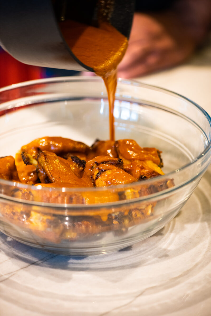 pouring homemade buffalo sauce on baked chicken wings