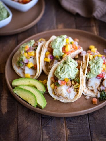 grilled fish tacos on a plate with sliced avocado