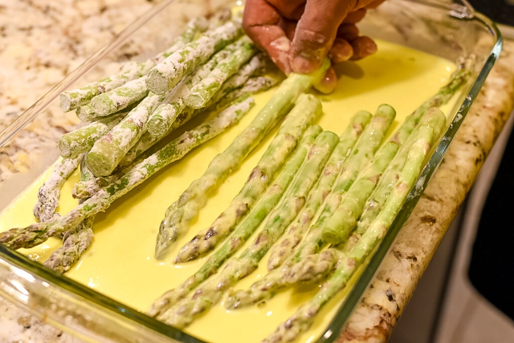 Dipping trimmed asparagus spears is egg batter.