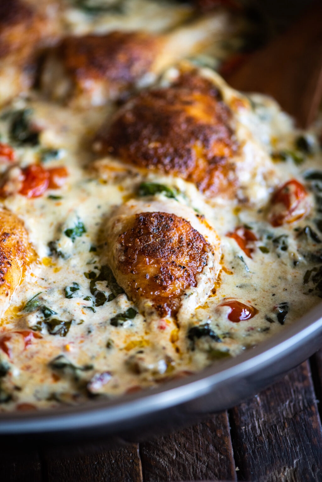 close up up a chicken drumstick in a creamy tuscan sauce with spinach and cherry tomatoes