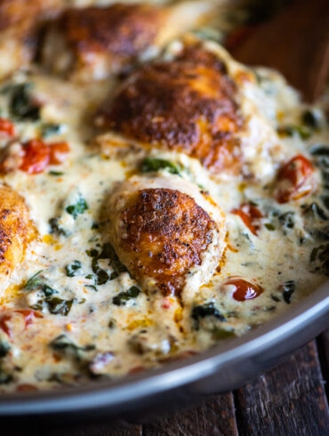 close up up a chicken drumstick in a creamy tuscan sauce with spinach and cherry tomatoes