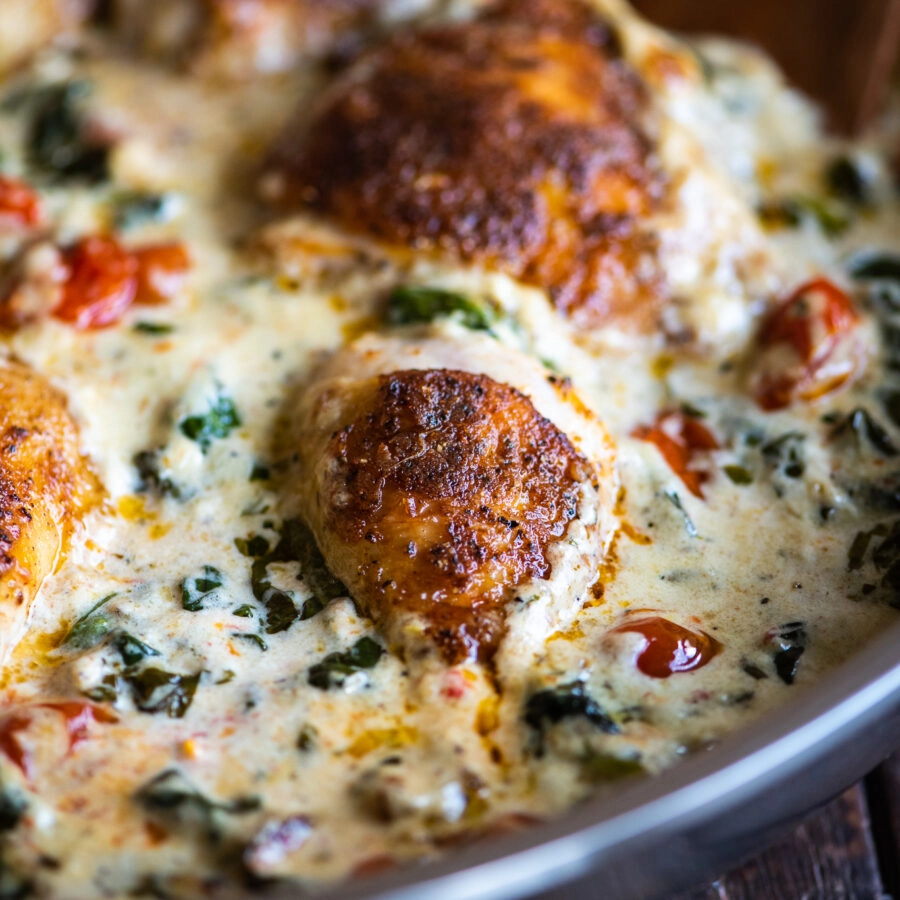 close up up a chicken drumstick in a creamy tuscan sauce with spinach and cherry tomatoes
