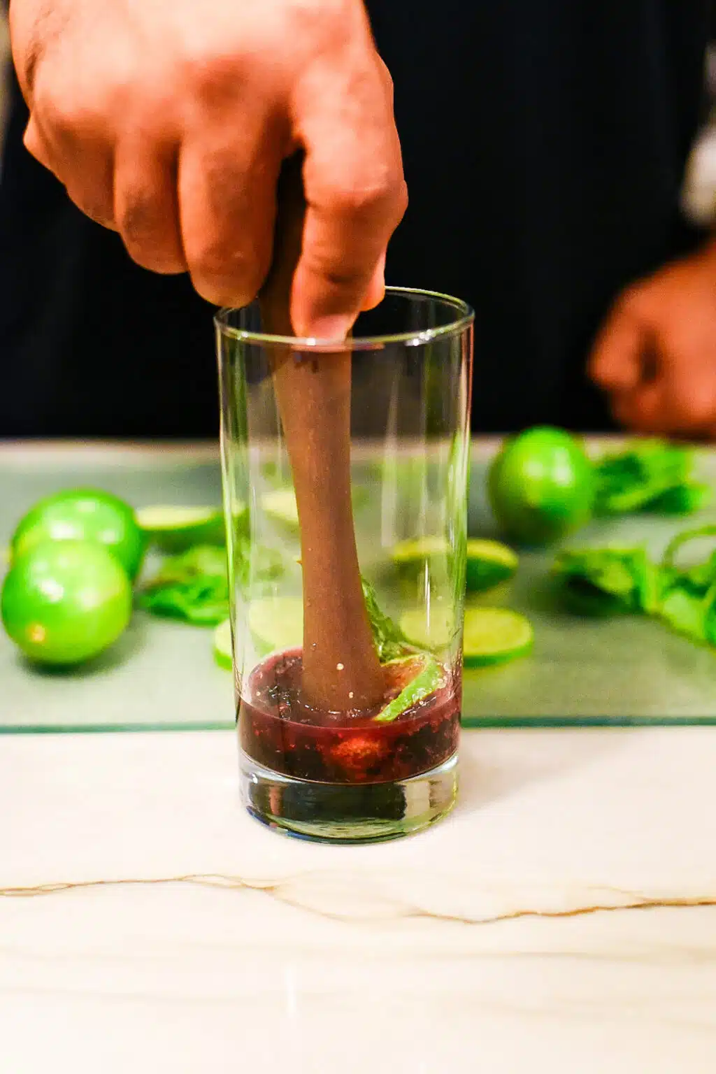 muddling the blackberries, sugar, mint leaves, and lime to make a blackberry mojito cocktail
