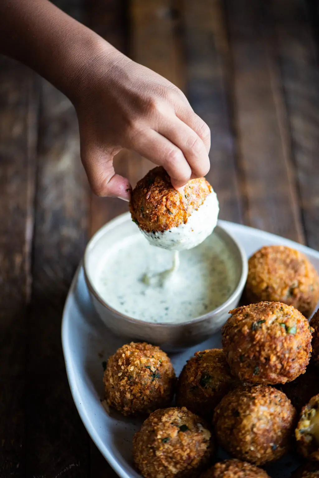 hand dipping arancini into pesto ranch dipping sauce