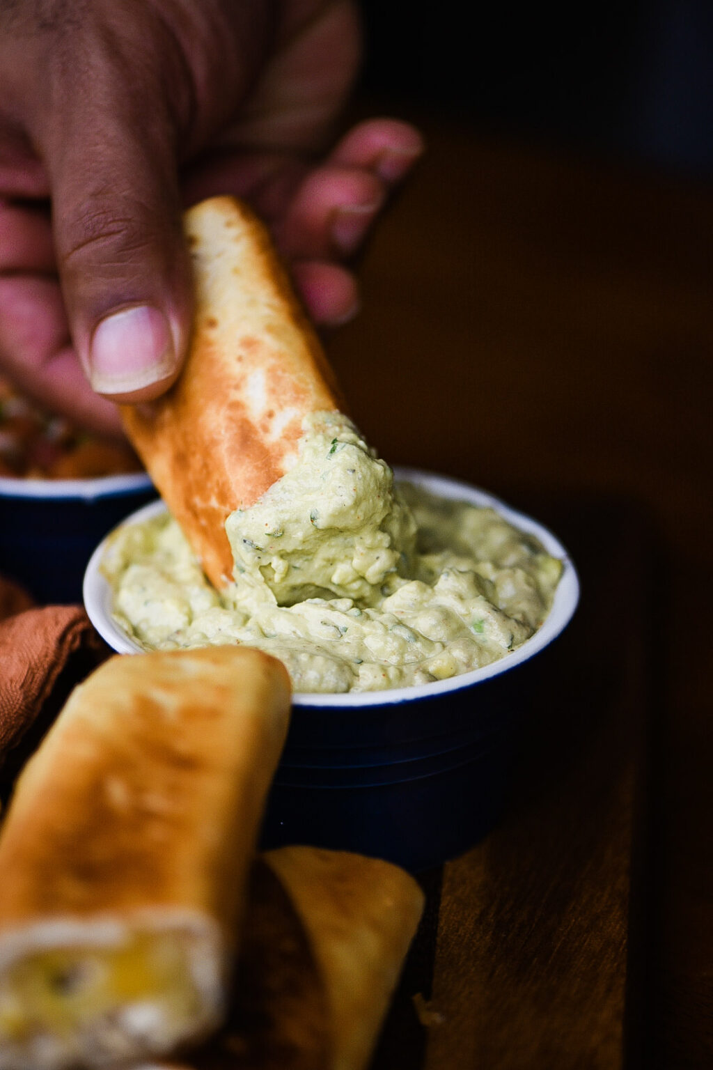 Dipping Shredded Chicken Flautas in avocado cream sauce