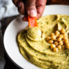 taking a dip of hummus with a raw red pepper