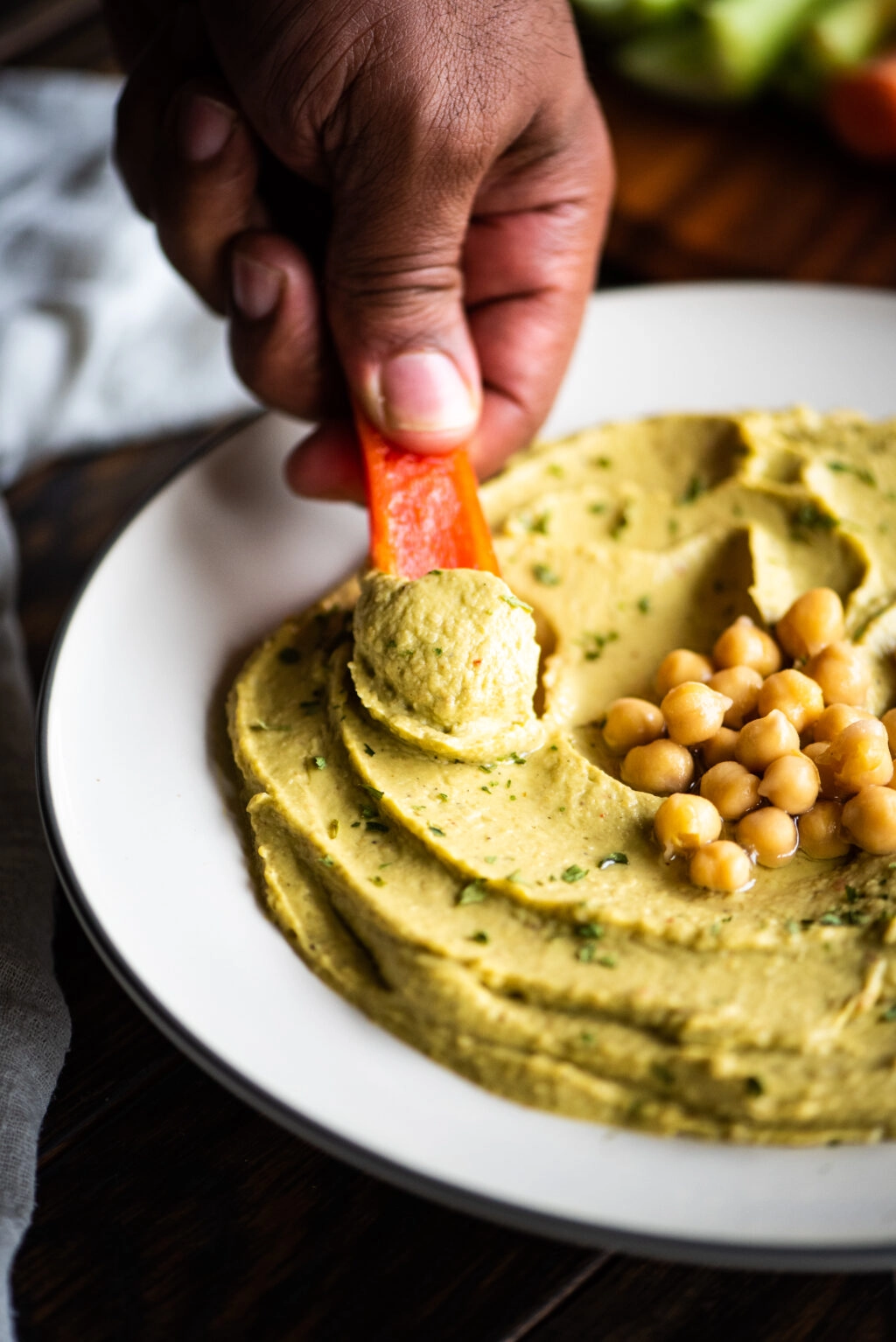 taking a dip of hummus with a raw red pepper