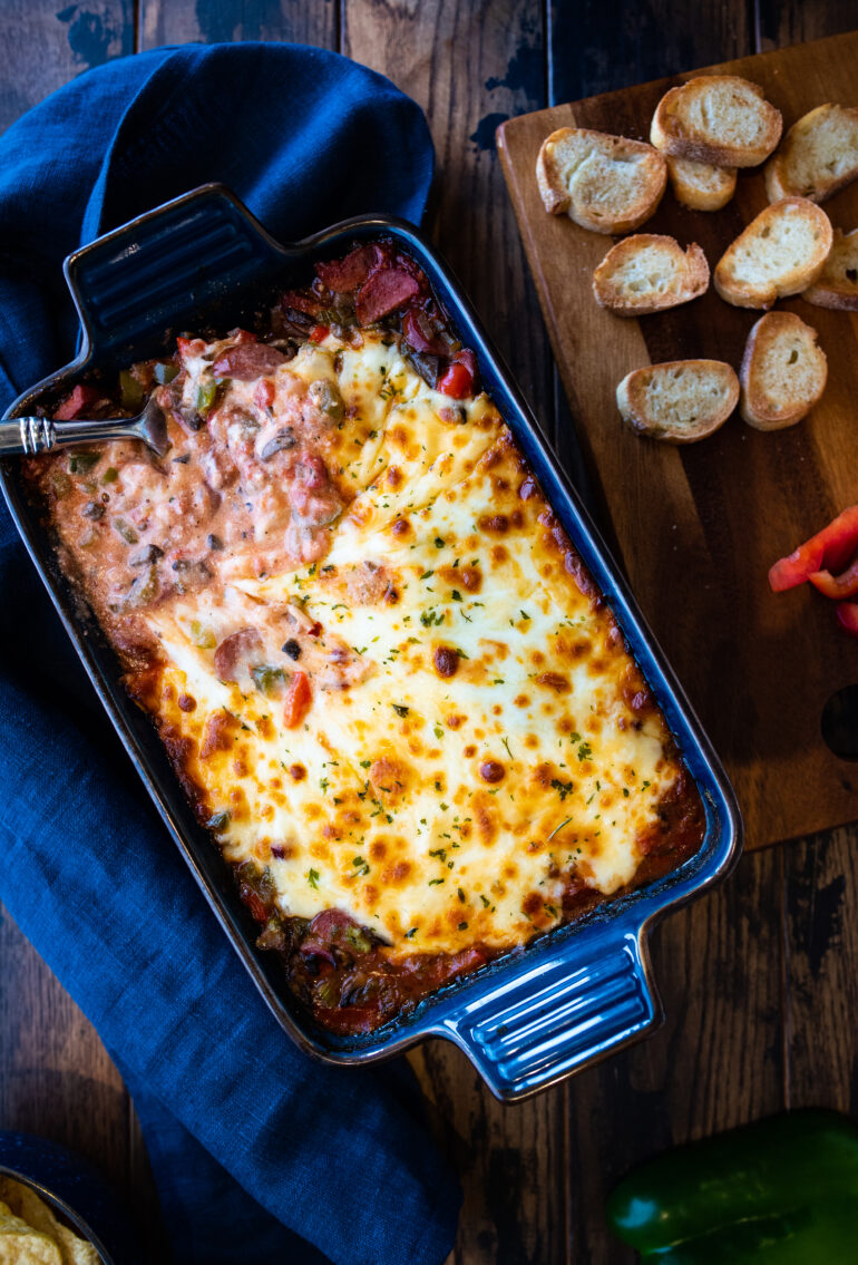 Overhead shot of sausage dip with a serving spoon and side of crostinis