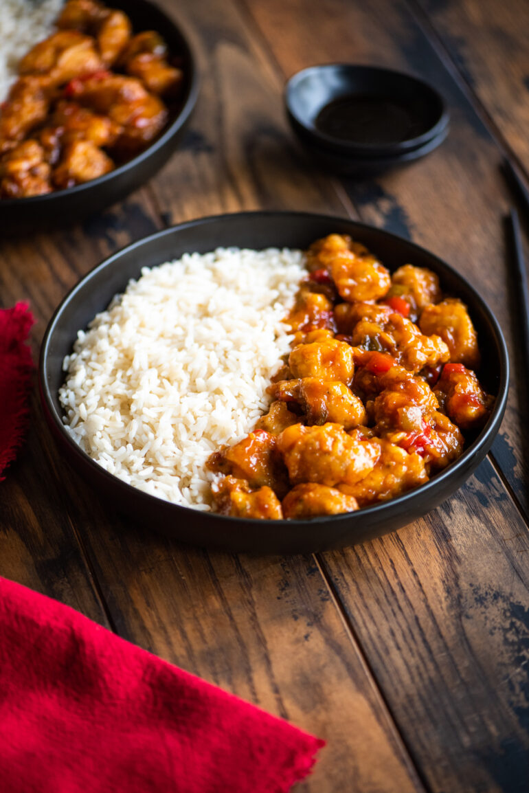 side shot of sweet and sour chicken served with rice and black chopsticks