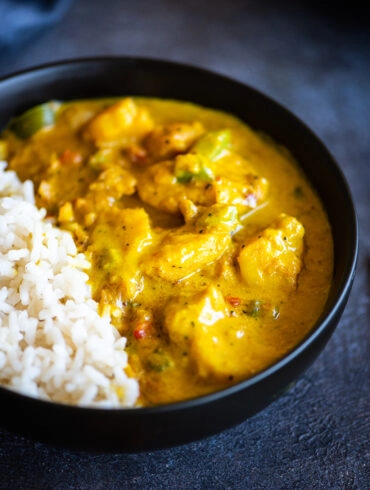 Close up of yellow fish curry served with white rice in a black bowl
