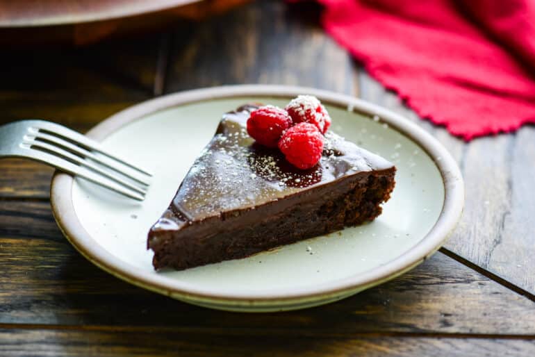 slice of flourless chocolate cake topped with raspberries and powdered sugar