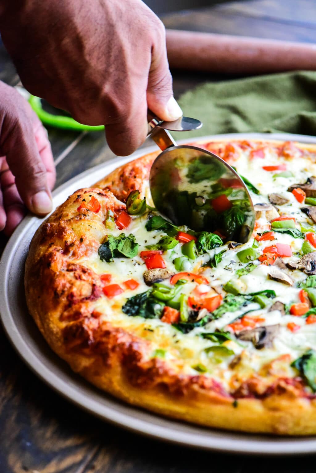 cutting a veggie pizza with a pizza cutter