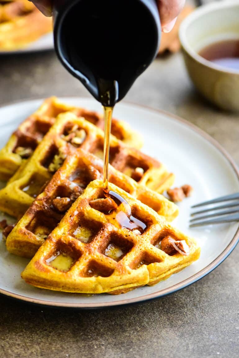 pouring maple syrup over pumpkin waffles