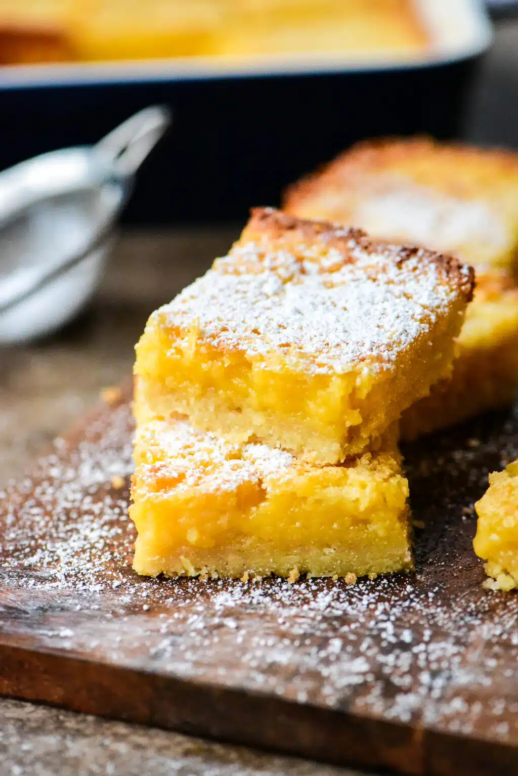 lemon bars stacked on a small wooden cutting board