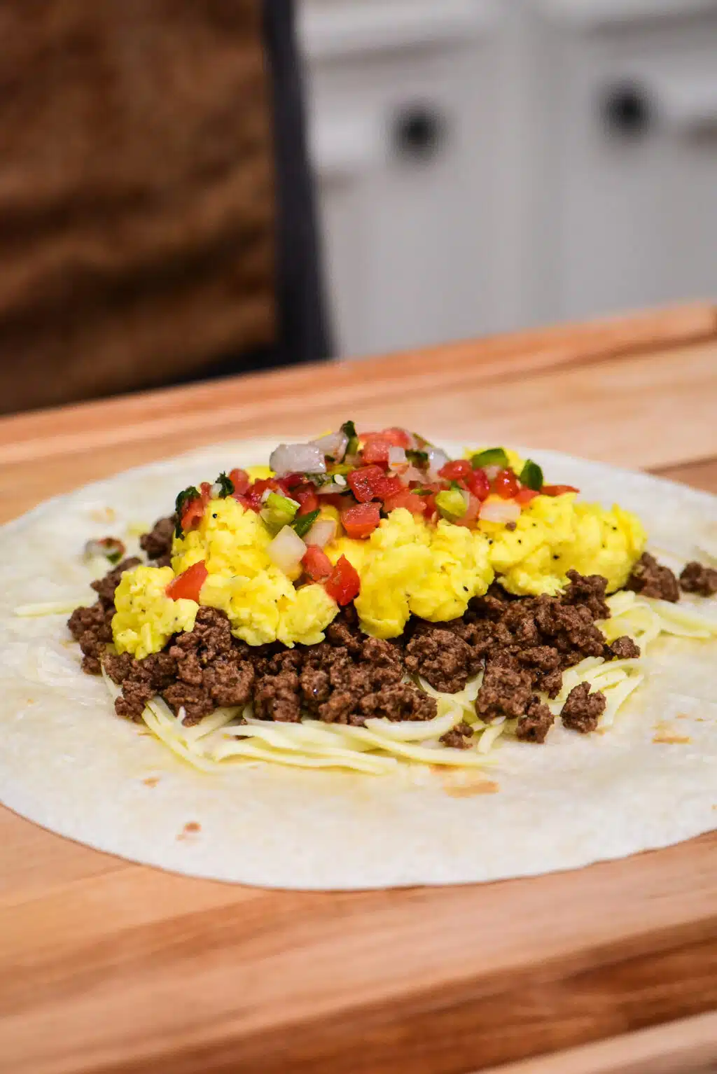 layering ingredients inside a large flour tortilla to make a beef breakfast burrito