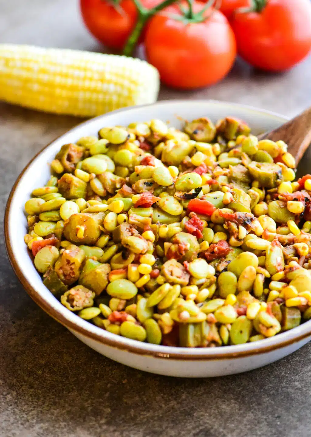 bowl of vegetarian succotash with whole corn and tomatoes in the background