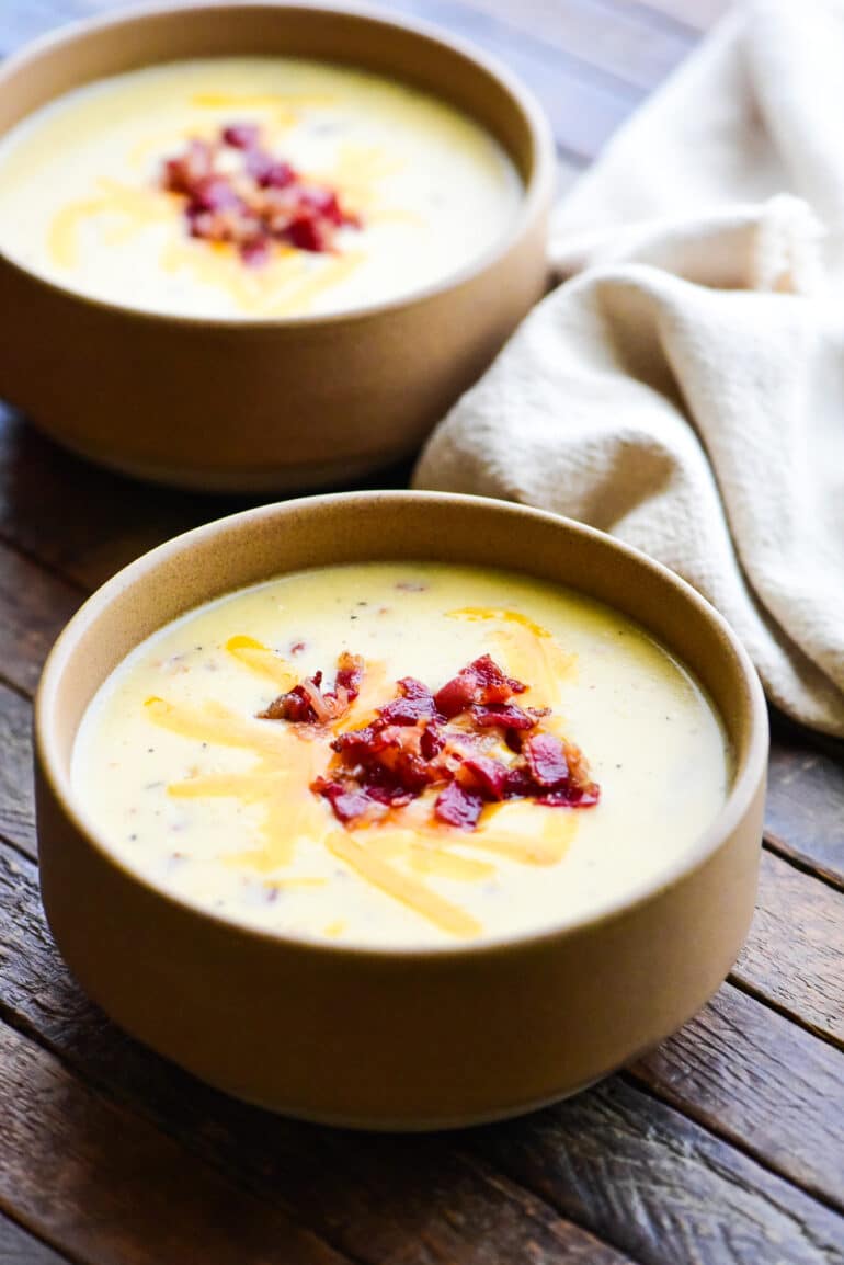 two bowls of baked potato soup topped with shredded cheese and bacon