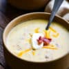 bowl of baked potato soup topped with shredded cheese and bacon