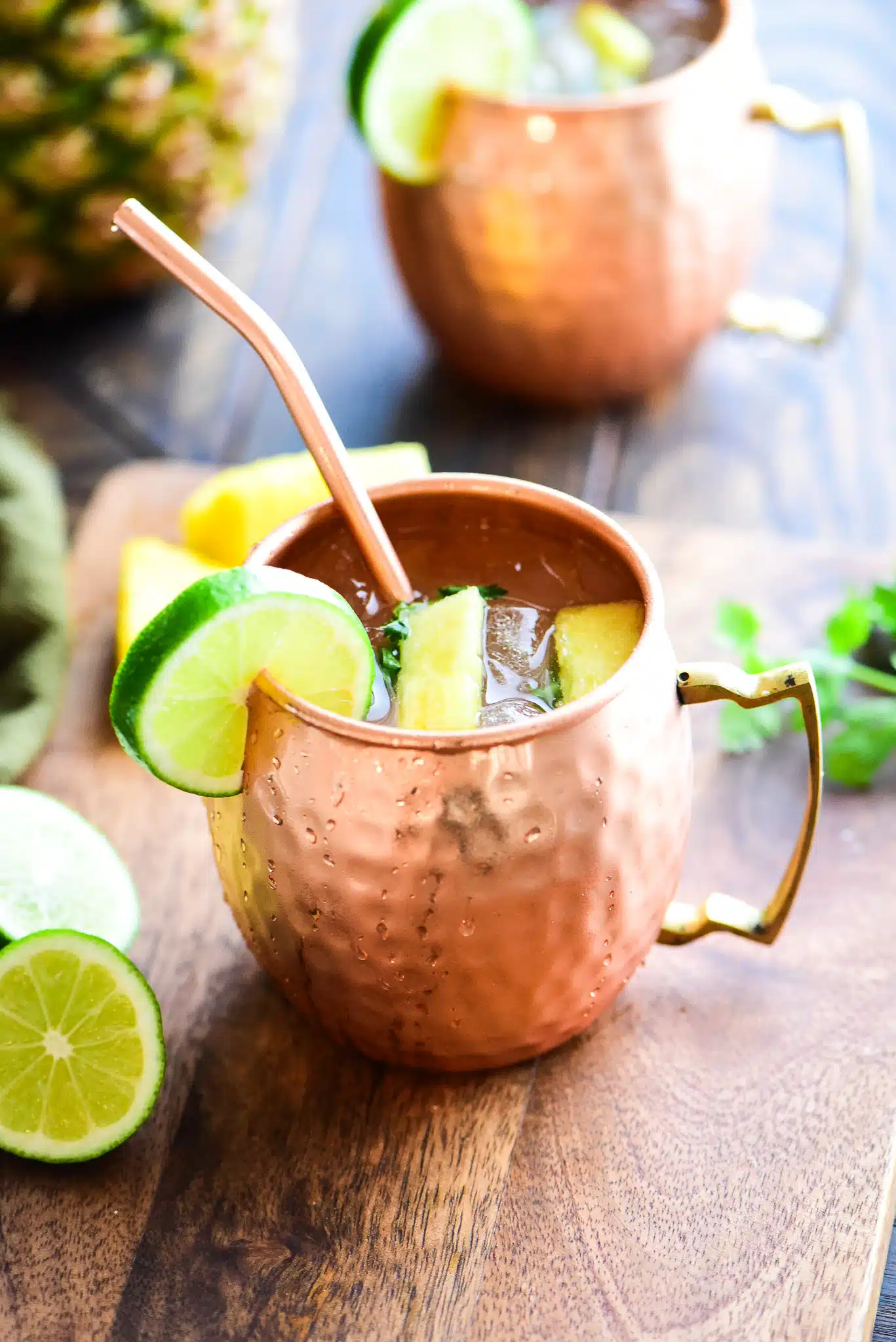 Pineapple Moscow Mule served in a copper mug with a copper straw and garnished with a lime.