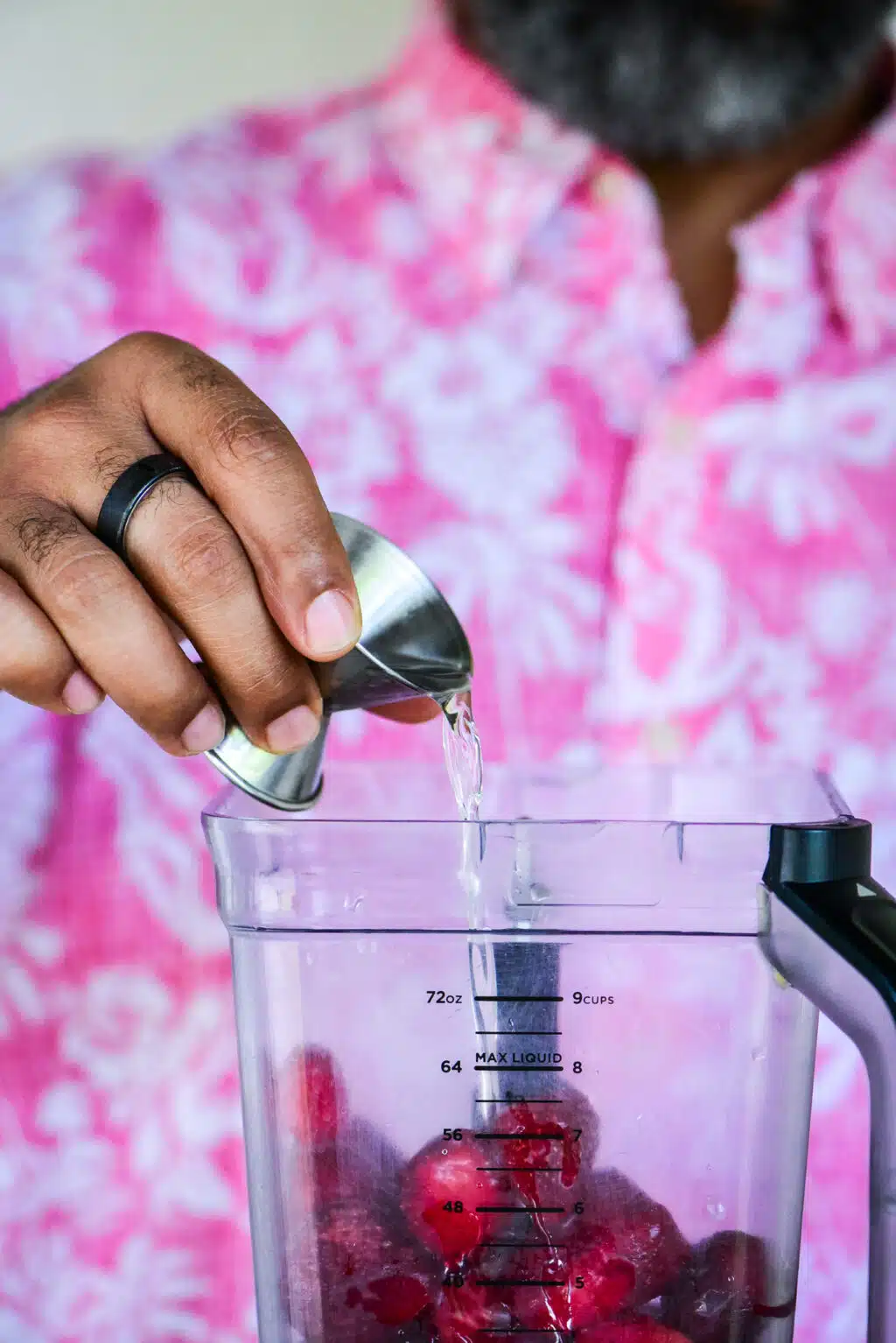 Adding white rum to a blender with frozen strawberries to make the strawberry daiquiri layer