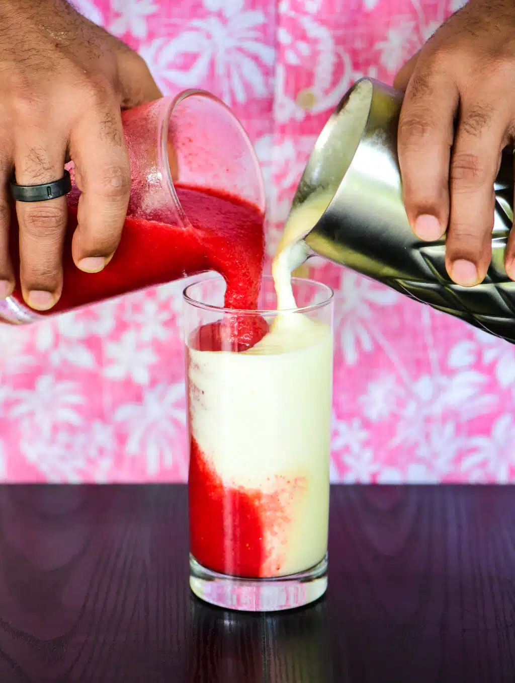pouring the pina colada and the strawberry daiquiri into the same glass at the same time.