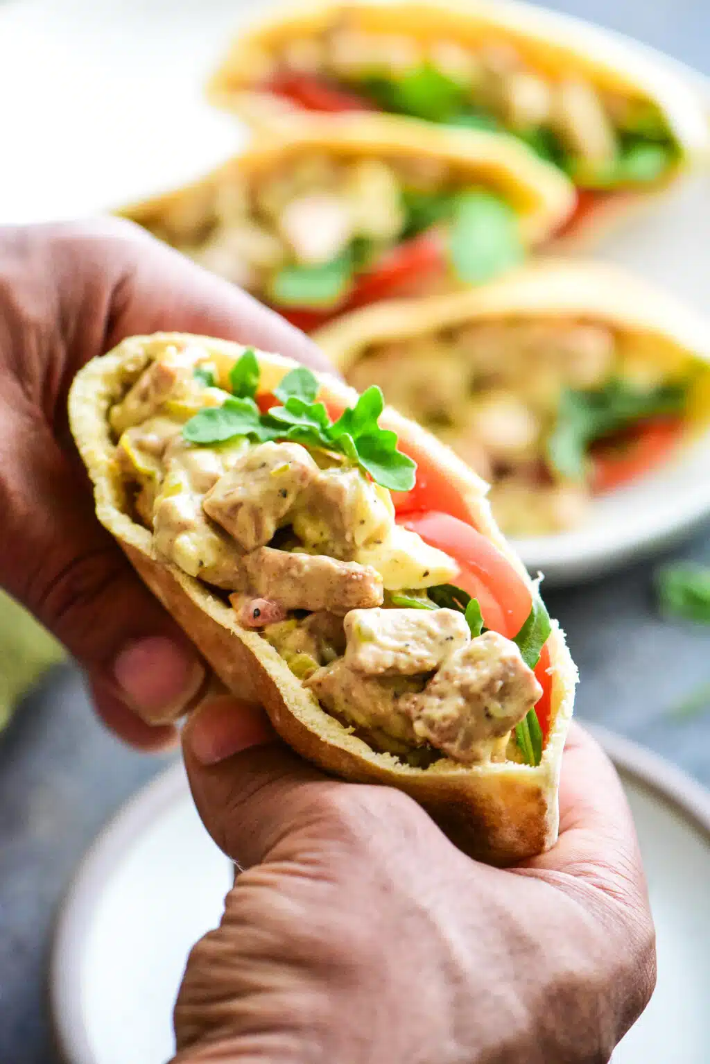 holding a single tuna salad pita pocket filled with tuna salad, arugula, and sliced tomato.