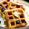 close up of a stack of lemon blueberry waffles drizzled with syrup