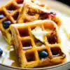 close up of a stack of lemon blueberry waffles drizzled with syrup