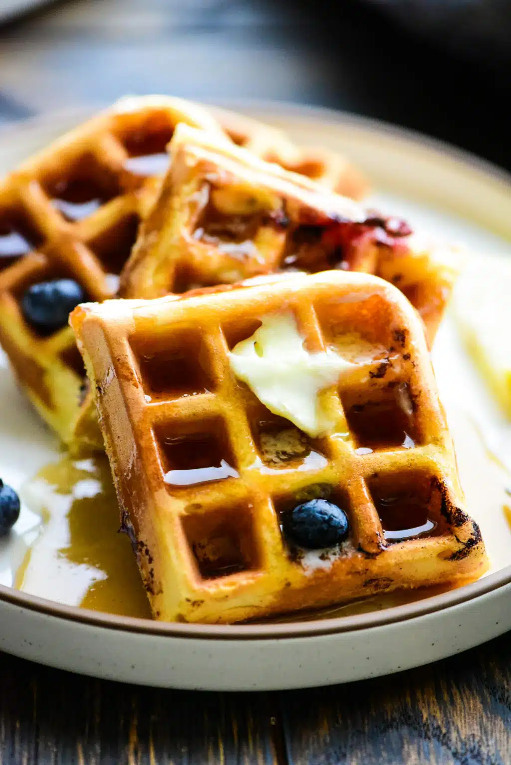 close up of a stack of lemon blueberry waffles drizzled with syrup