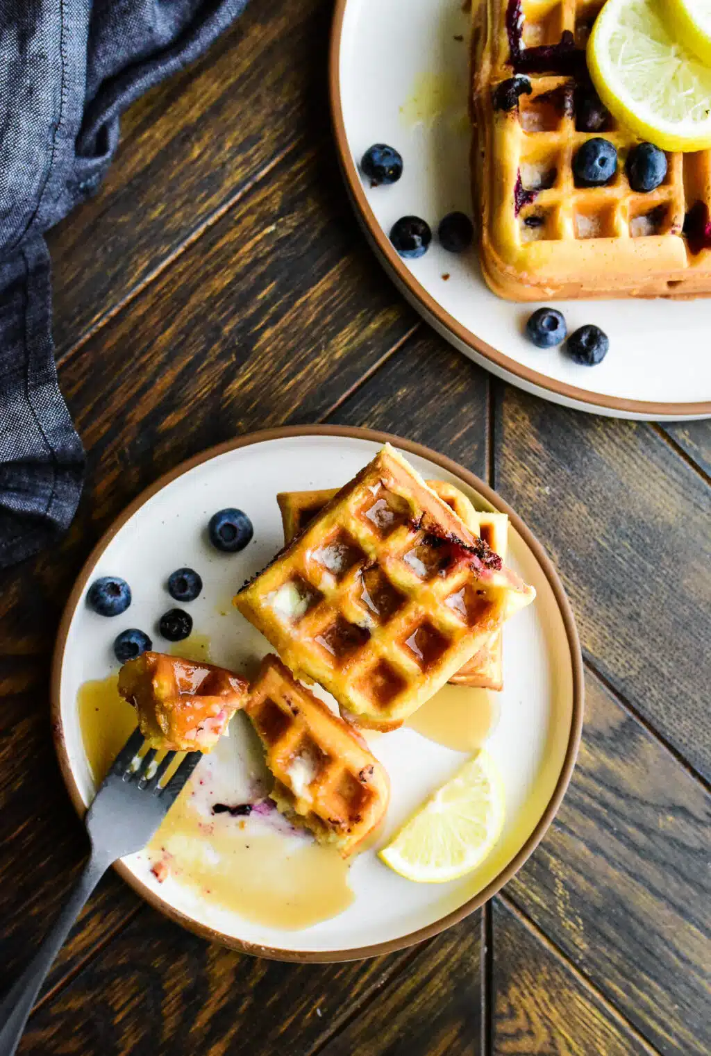 overhead shot of plate of lemon blueberry waffles drizzled with maple syrup with a bite taken out of it