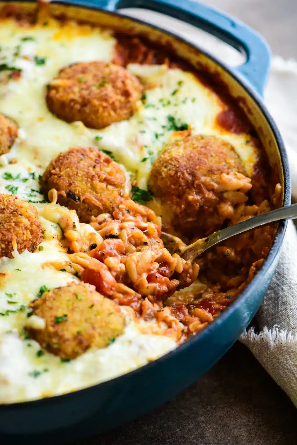 large skillet of chicken parmesan meatball orzo with a serving scooped out.