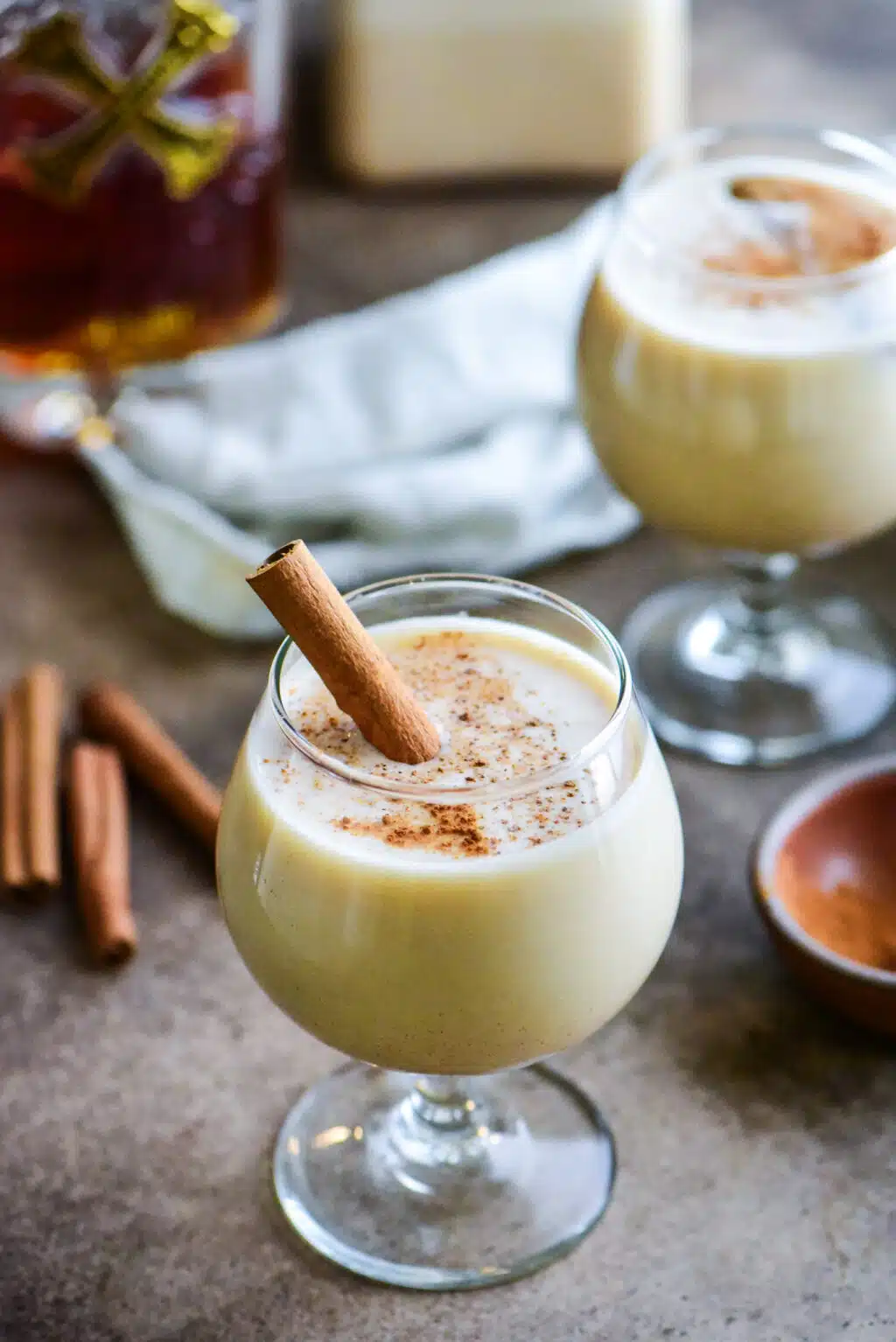 two coquito cocktails with a container of puerto rican coquito and dark rum in the background